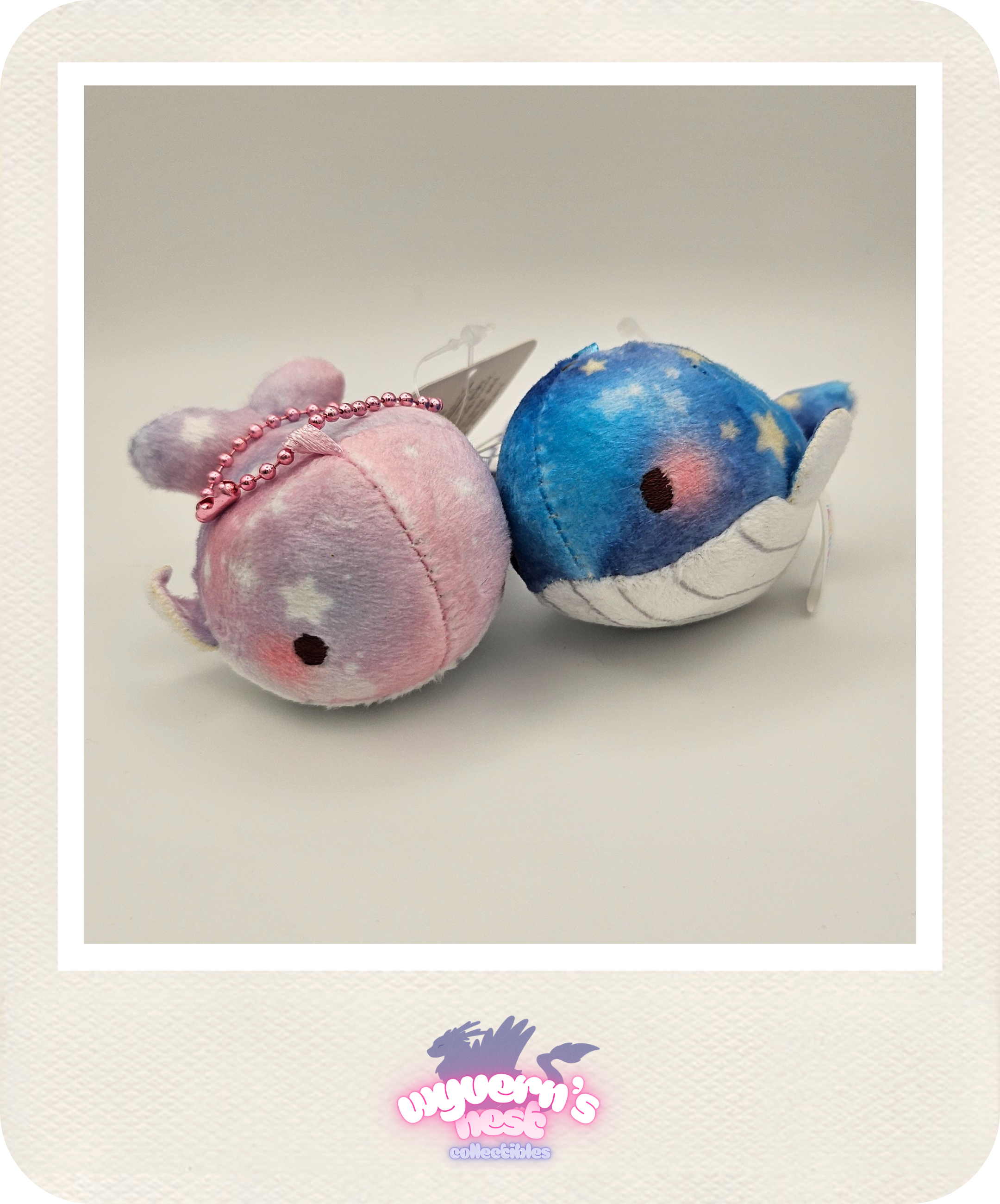 Two plush whale toys, one pink and one blue with star patterns, on a light gray background.