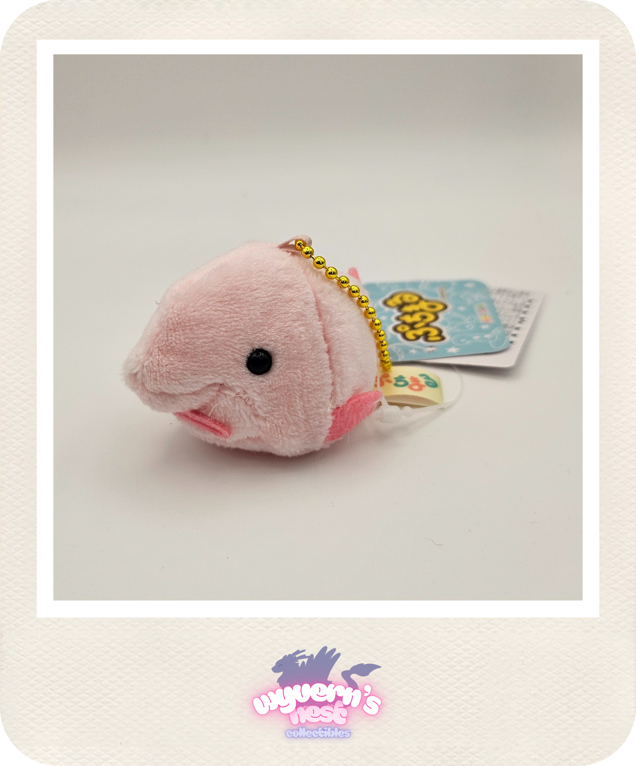 Pink plush fish charm with a tag on a light gray background